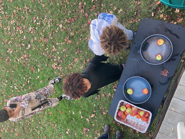 Photo of two boys bobbing for apples outside while a third boy waits for his turn