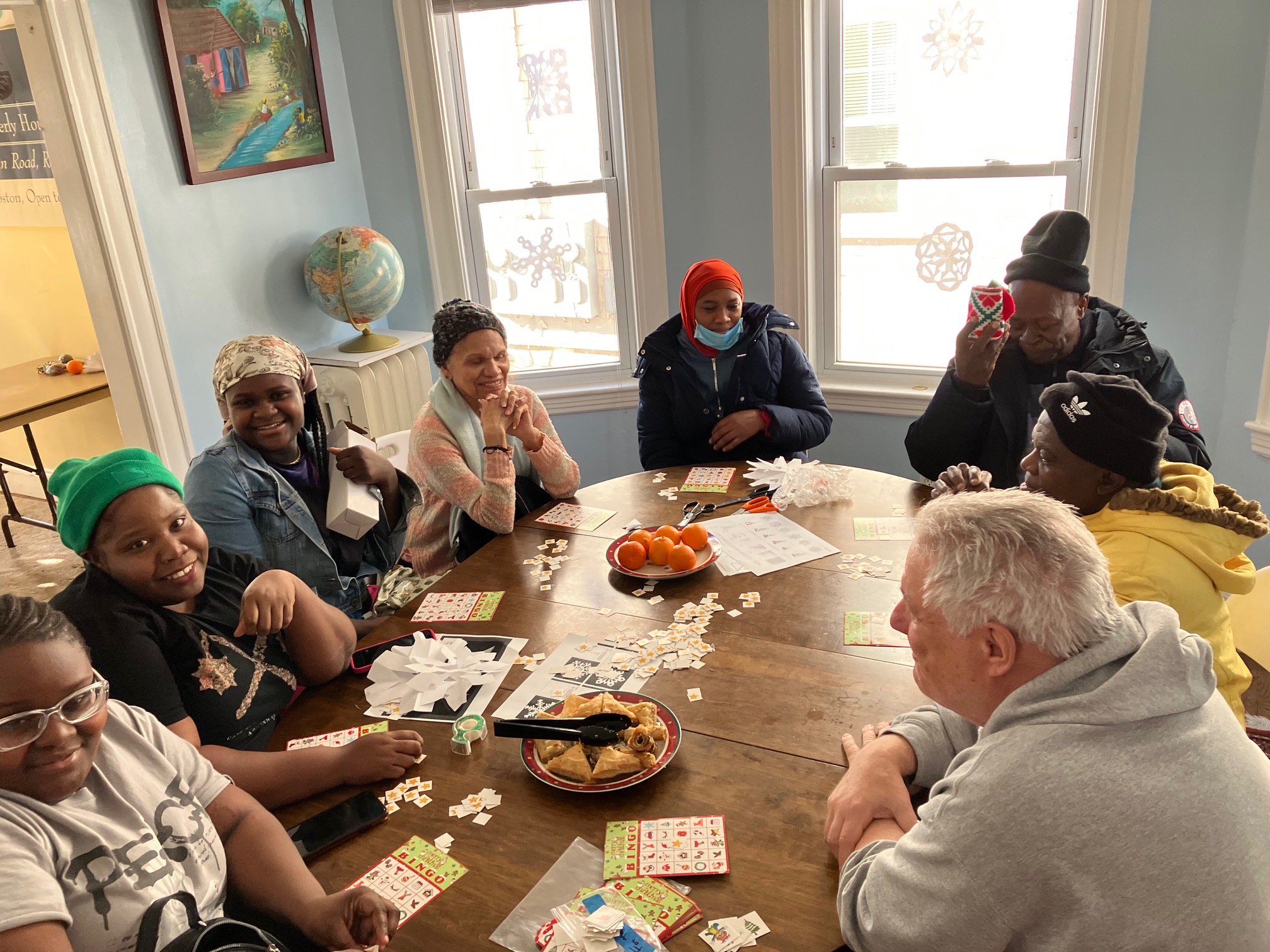 Photo of adult immigrants and their English instructor gathered around a table, playing BINGO.